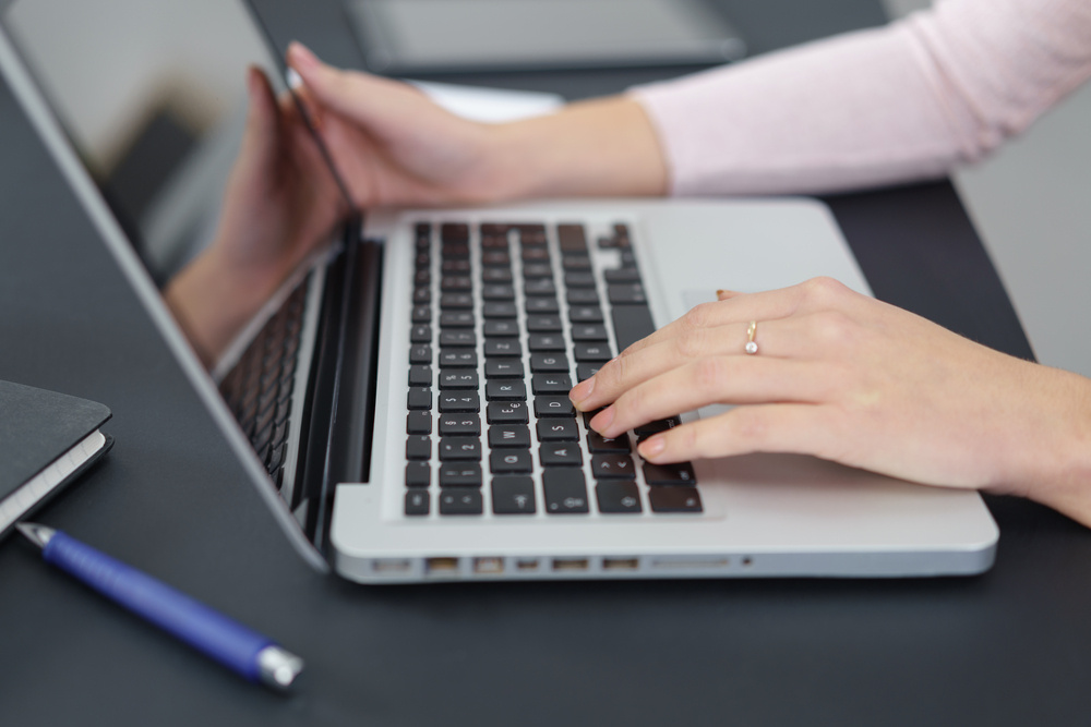 close-up of womans hands working on her laptop at the desk